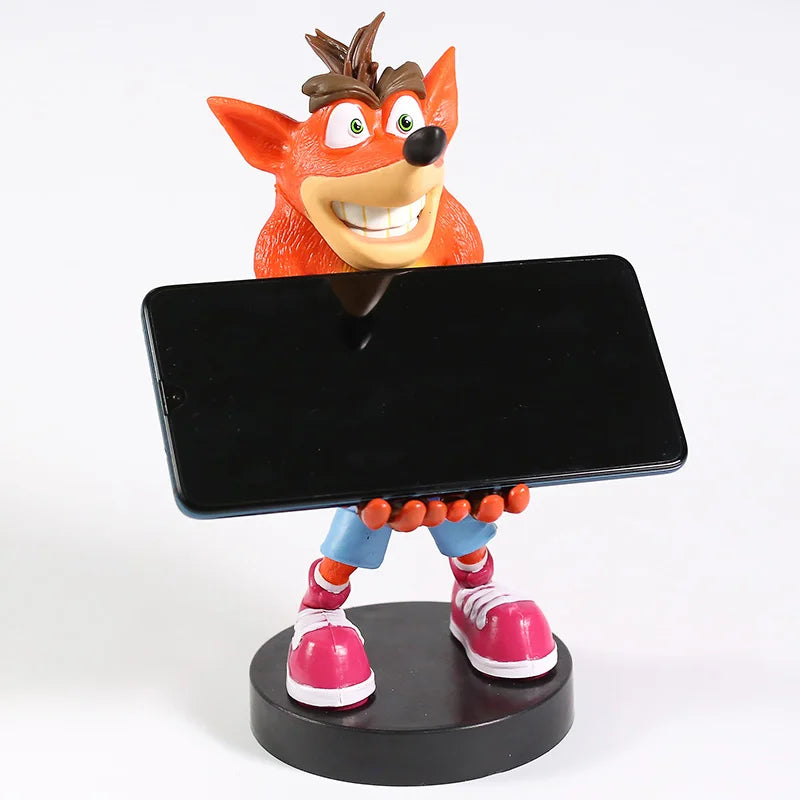 Figurine Crash Bandicoot™ en PVC de 22 cm tenant un smartphone noir, sur socle rond. Support manette ou téléphone, accessoire gaming rétro original.