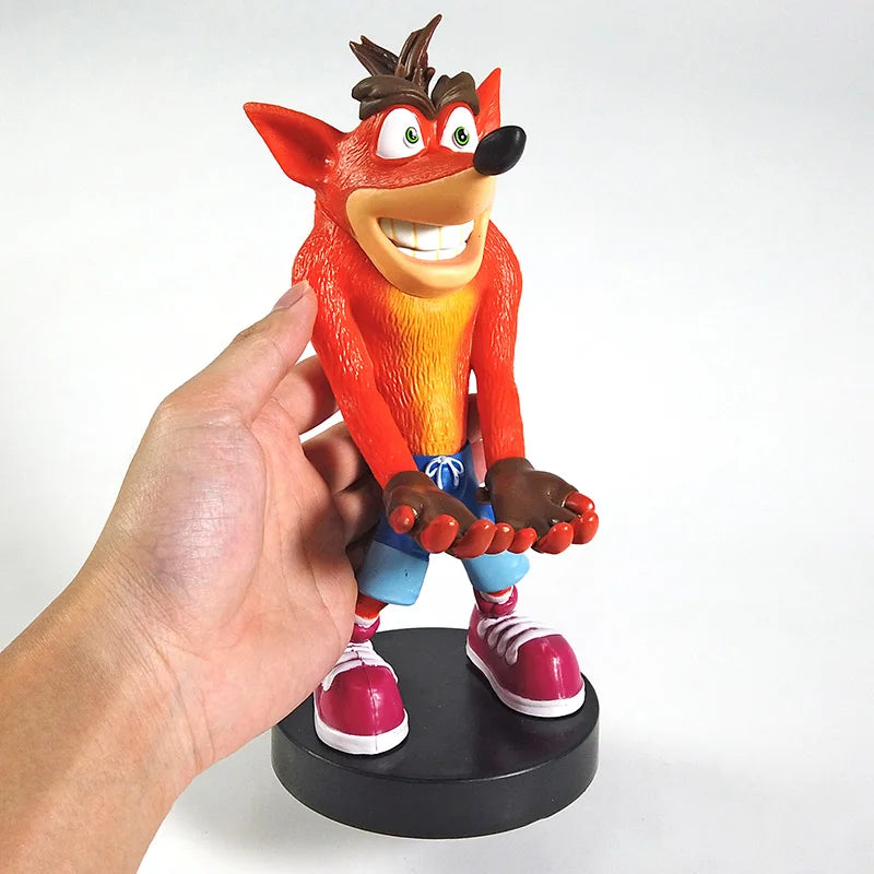 Main tenant la figurine Crash Bandicoot™ de 22 cm, support manette ou smartphone en PVC. Présentation du format réel pour visuel produit e-commerce.
