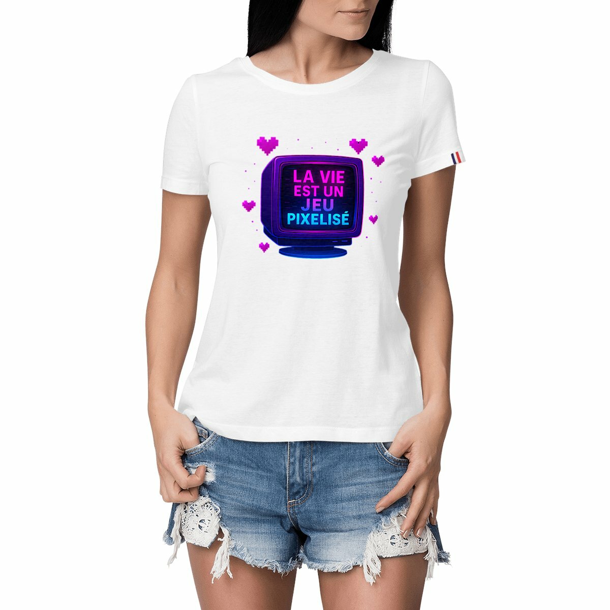 Femme portant un t-shirt blanc avec un visuel rétro pixel art et l’inscription « LA VIE EST UN JEU PIXELISÉ » sur un écran cathodique entouré de cœurs roses.