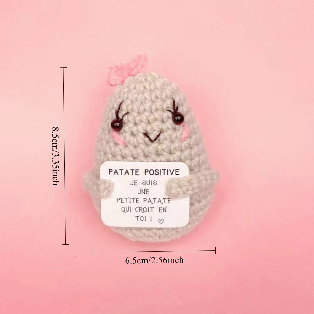 Peluche Patate Positive grise claire au crochet avec joues roses et petit nœud, tenant une pancarte motivation, taille 8,5 cm.