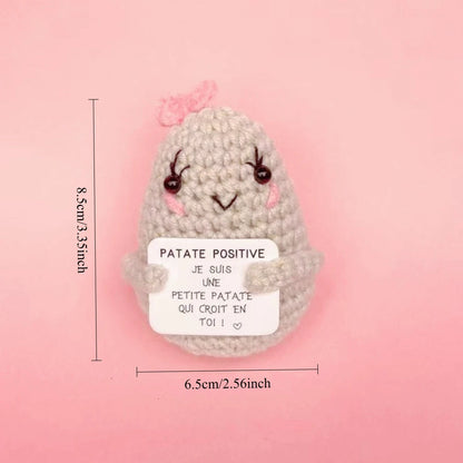 Peluche Patate Positive grise claire au crochet avec joues roses et petit nœud, tenant une pancarte motivation, taille 8,5 cm.