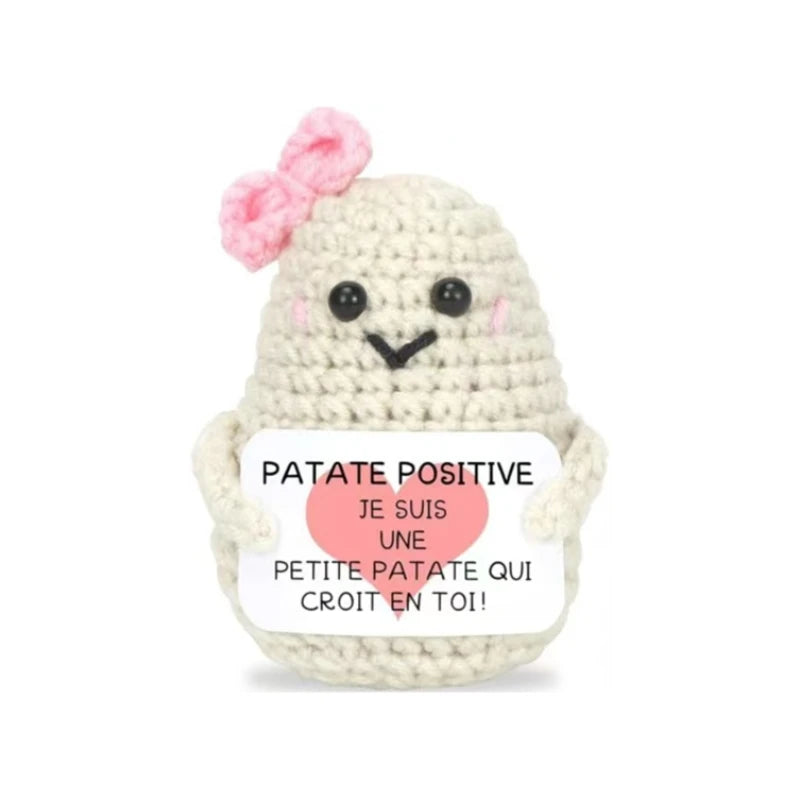 Peluche Patate Positive blanche au crochet avec nœud rose, tenant une pancarte “Je suis une petite patate qui croit en toi”, idée cadeau mignonne.