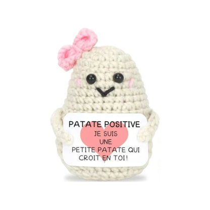 Peluche Patate Positive blanche au crochet avec nœud rose, tenant une pancarte “Je suis une petite patate qui croit en toi”, idée cadeau mignonne.
